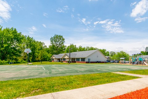 a basketball court in front of a building with a playground in the background