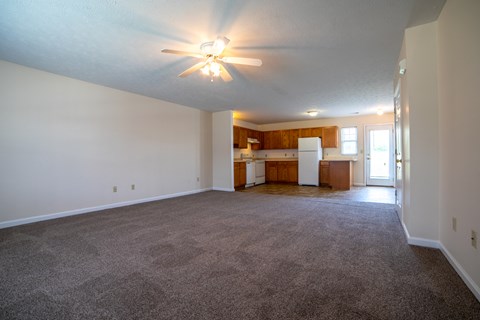 an empty living room with a kitchen in the background