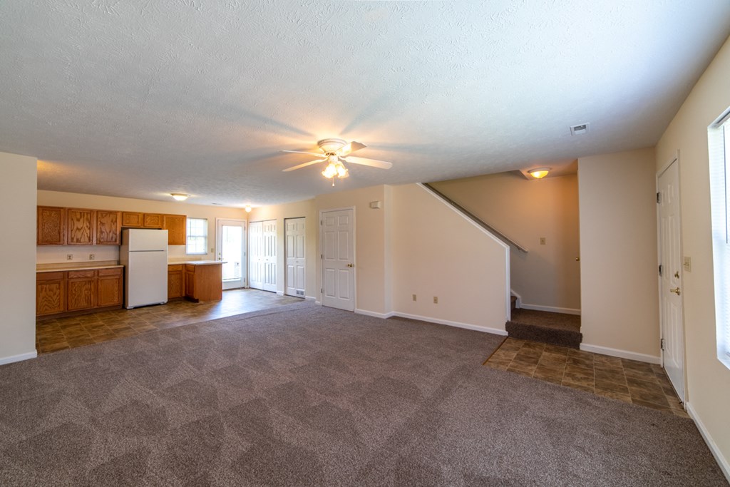 an empty living room with a kitchen in the background