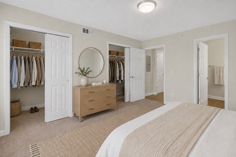 A bedroom with a large bed and a closet with clothes hanging.