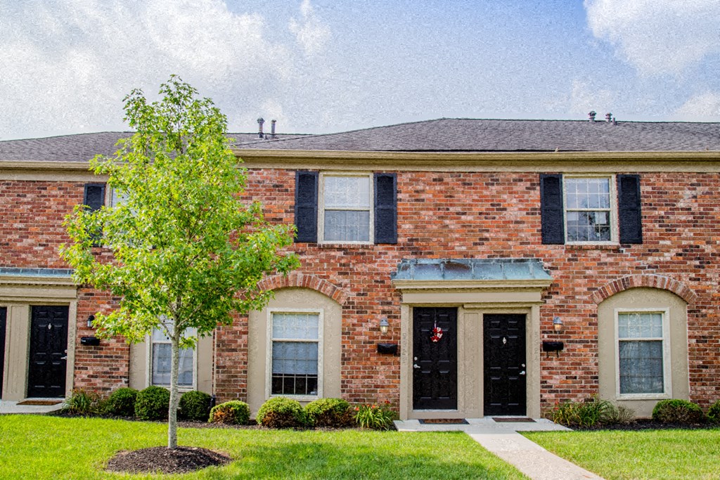 the front of a brick house with a tree in the yard