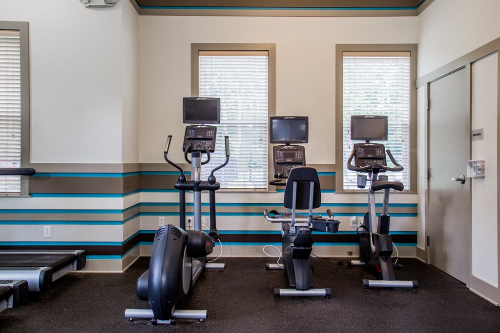 a gym with three exercise machines and two windows