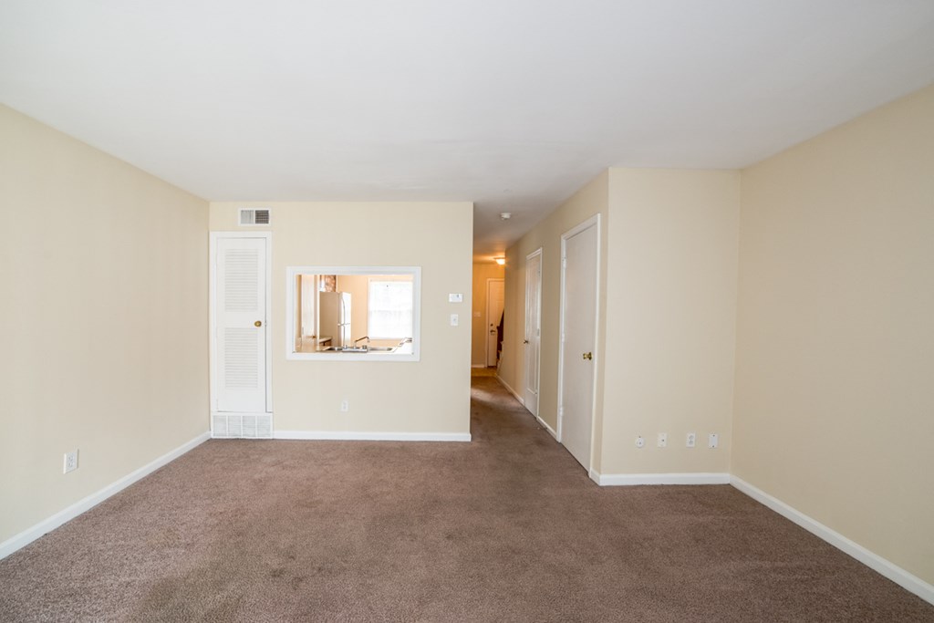 an empty living room with carpet and a hallway to a bedroom