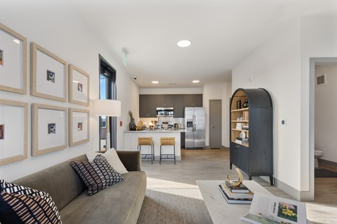 Model apartment living room with modern sofa, curated wall art, open kitchen with island seating, stainless steel appliances, and contemporary finishes at Montage