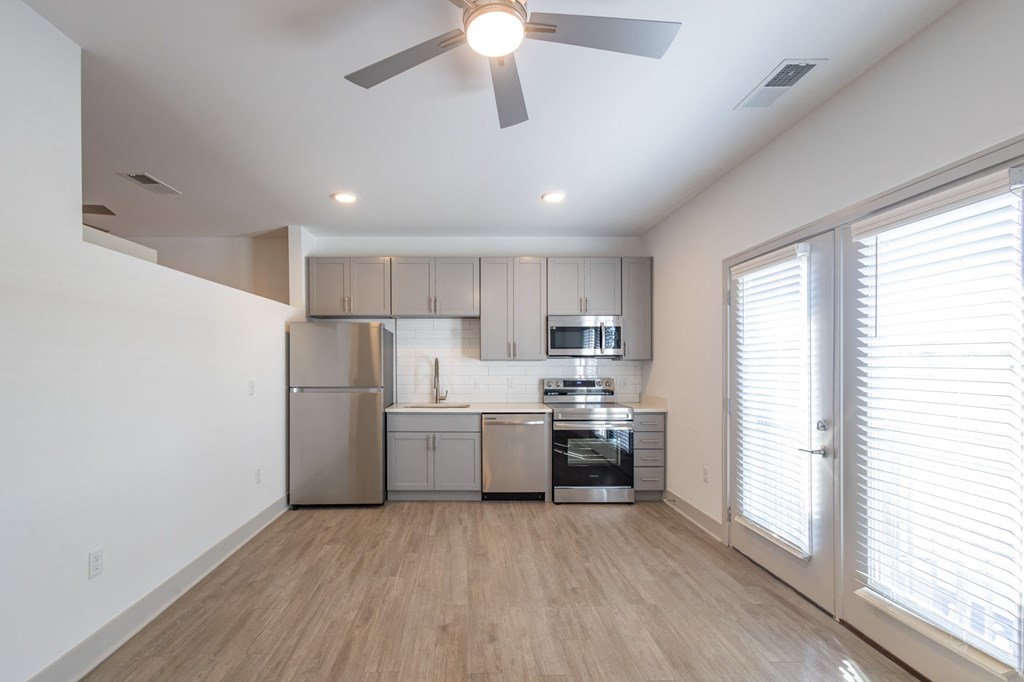 an empty living room with a kitchen with a ceiling fan