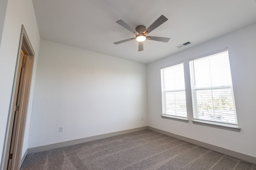 an empty living room with a ceiling fan and two windows