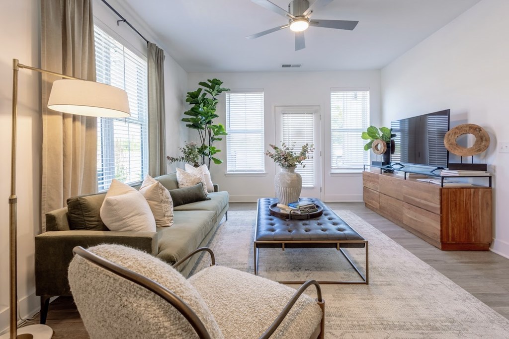 Bright living room with green sofa, TV console, and large windows i