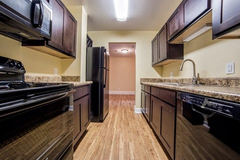 A kitchen with black appliances and wooden floors.