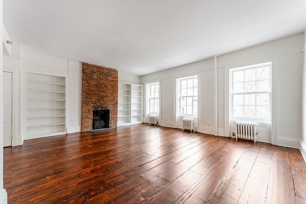 an empty living room with hardwood floors and a brick fireplace
