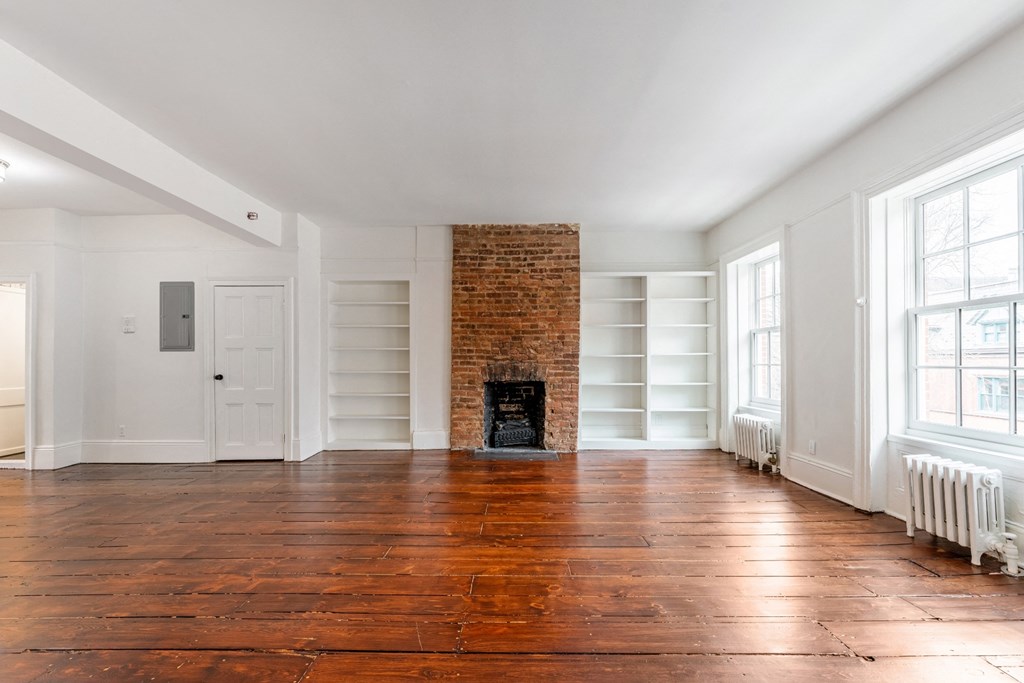 an empty living room with a brick fireplace and white bookshelves