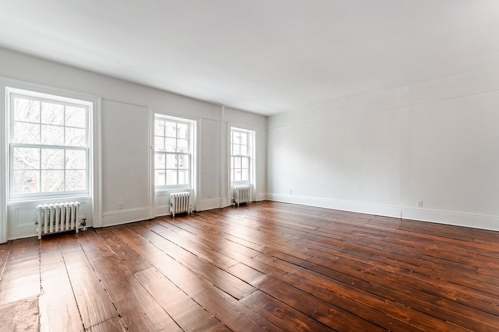 an empty room with hardwood floors and three windows