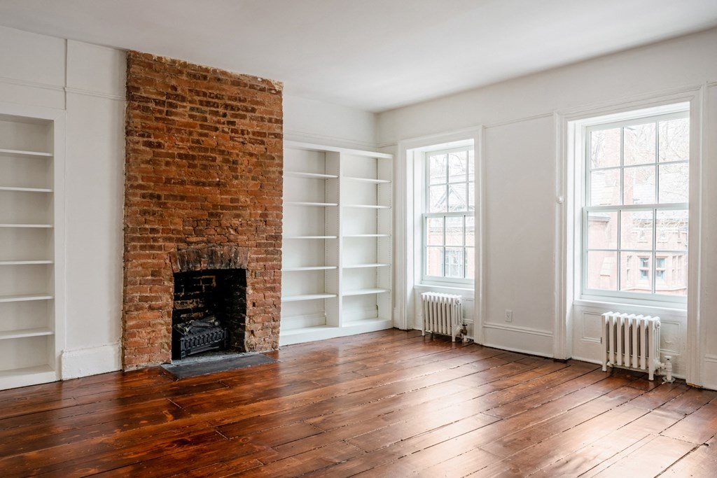 an empty room with a brick fireplace and white bookshelves