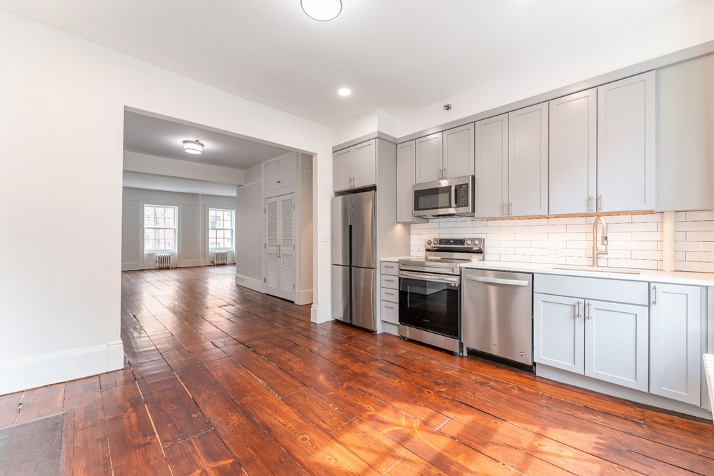 a kitchen and living room with white cabinets and wood floors