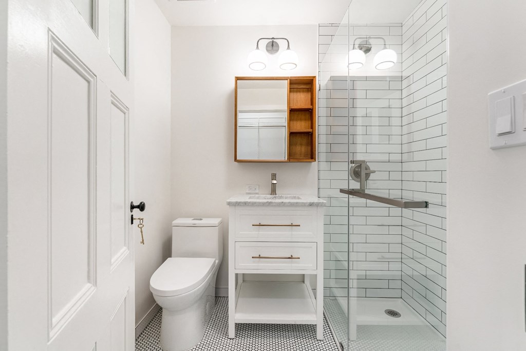 a bathroom with white walls and a white toilet next to a walk in shower with a glass