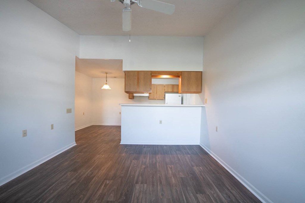an empty living room with a kitchen in the background