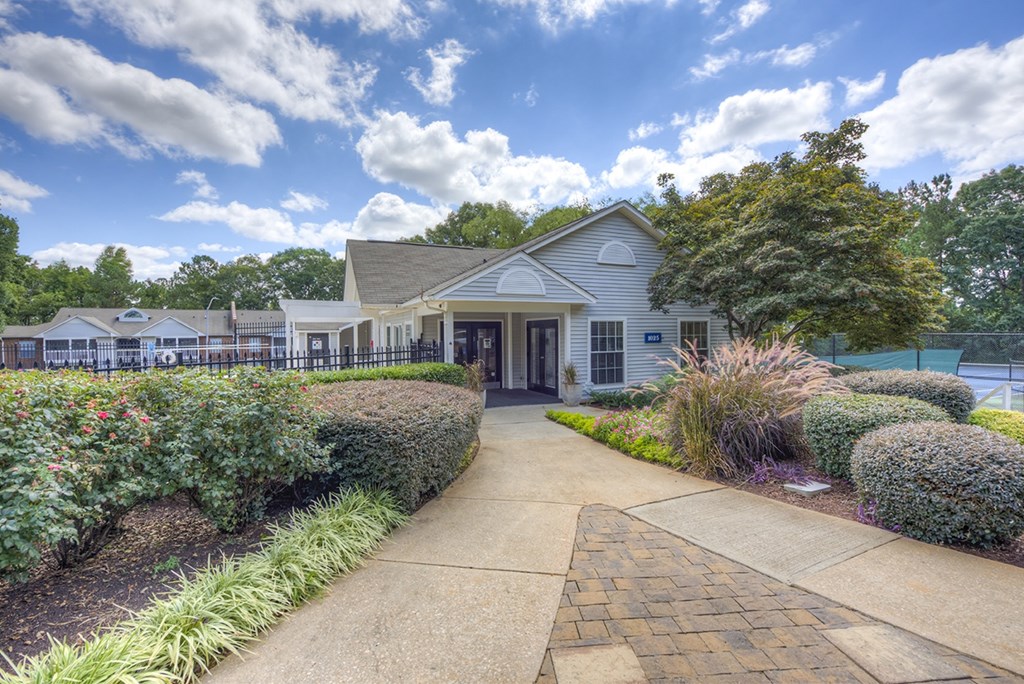 A white building with a brown roof is surrounded by green bushes and trees.