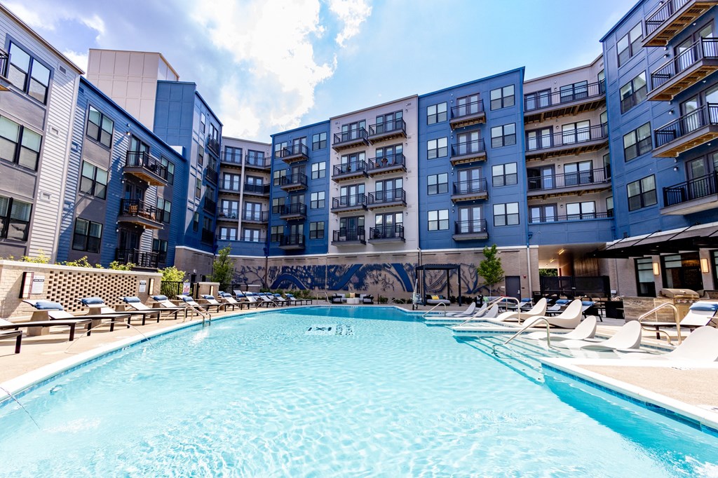 a large swimming pool with chaise lounge chairs and a building in the background