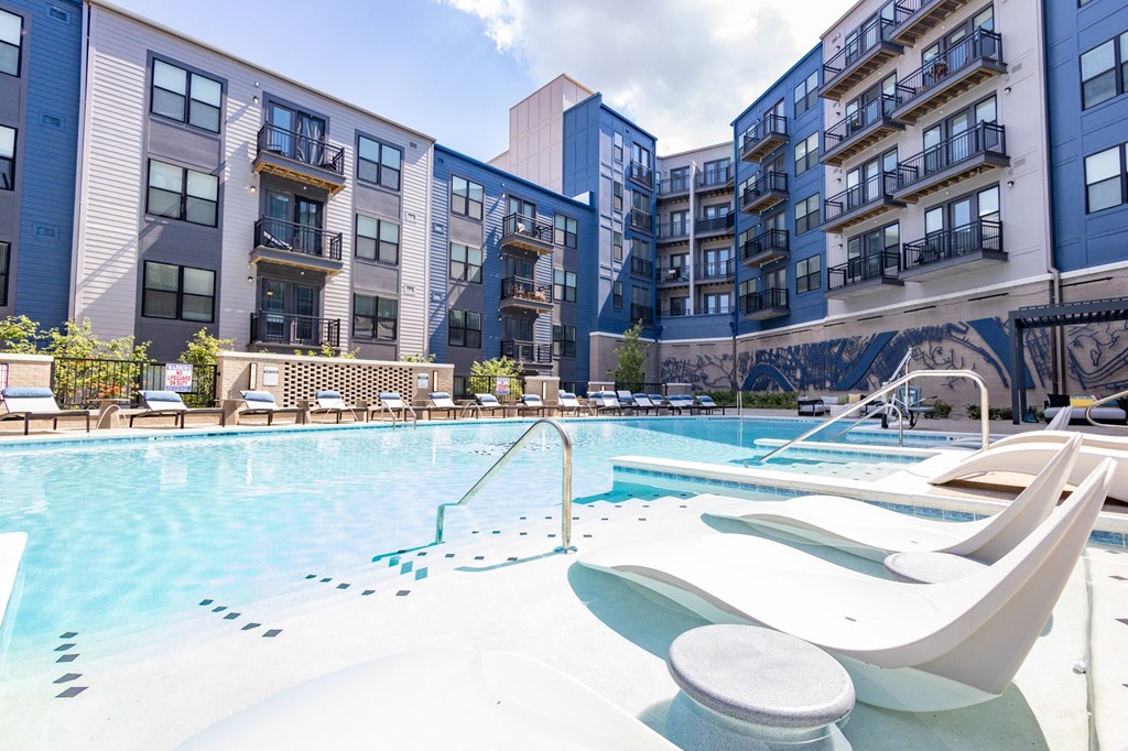an outdoor swimming pool with chaise lounge chairs and an apartment building in the background