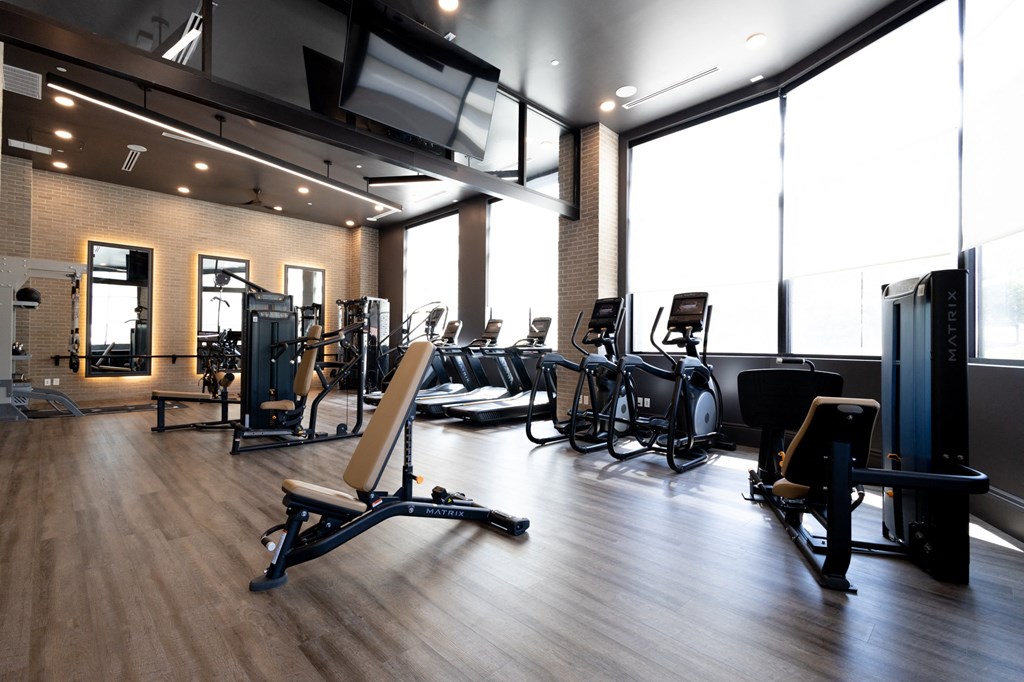a large fitness room with cardio equipment and windows