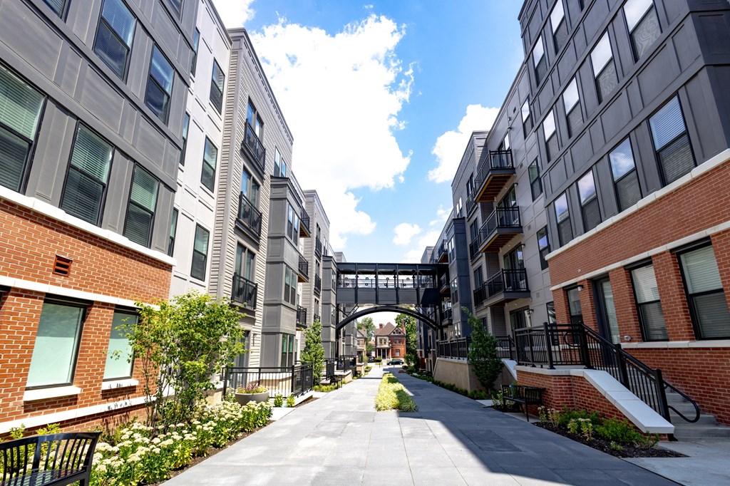 a walkway between two apartment buildings with a bridge in the background