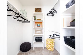 a walk in closet with white walls and shelves and a staircase with black and white