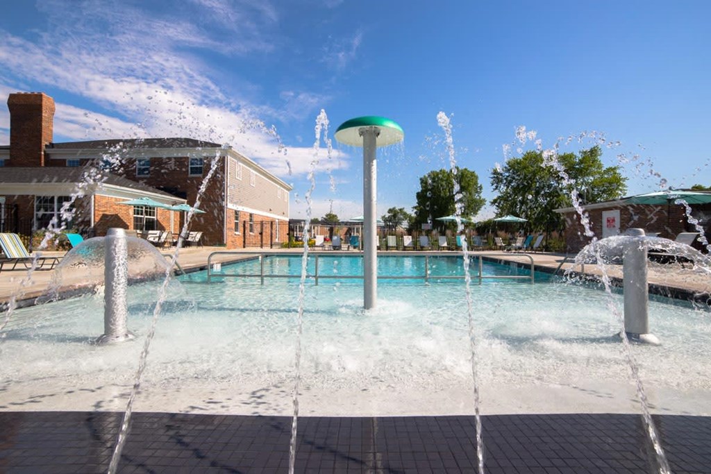 a pool with water sprinklers and a building in the background