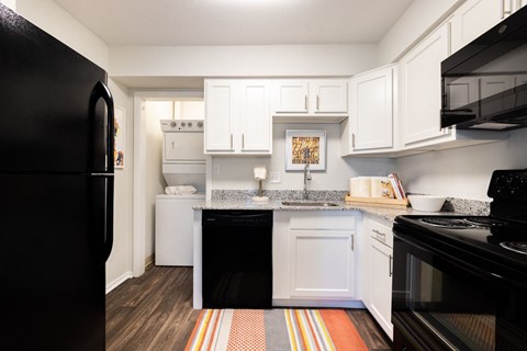 A black refrigerator is on the left in a kitchen with white cabinets.