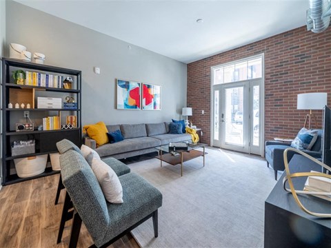 A living room with a grey couch, a grey chair, a black bookshelf, and a painting on the wall.