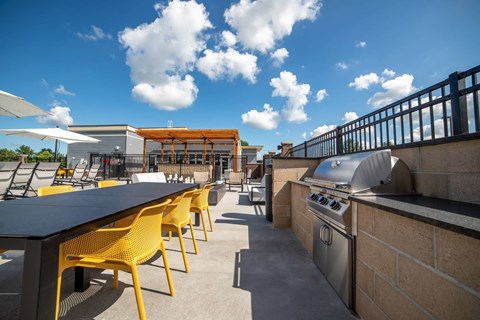 a patio with a grill and tables with yellow chairs at The Century at Purdue Research Park-Student, West Lafayette, 47906