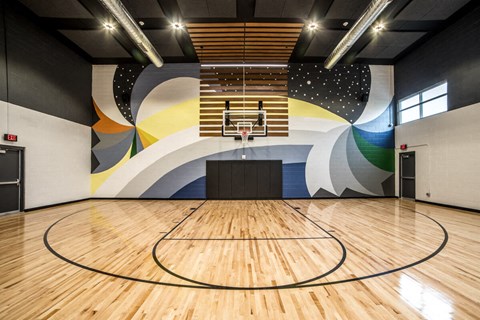 a basketball court in a gym with a colorful mural on the wall at The Century at Purdue Research Park-Student, Indiana