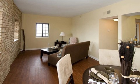 A living room with a brown couch, a coffee table, and a dining table set for two.