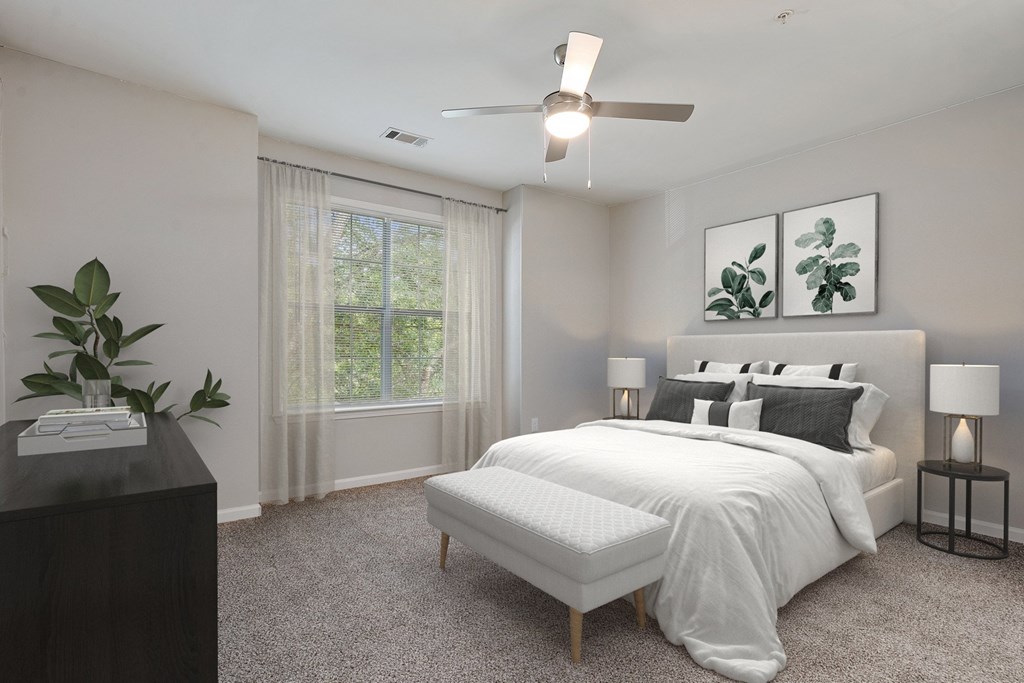 A bedroom with a large bed, a ceiling fan, and a plant on a table.
