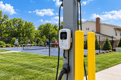 A parking meter on a pole with a tennis court in the background.