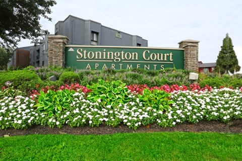 A sign for Stonington Court Apartments is surrounded by flowers.