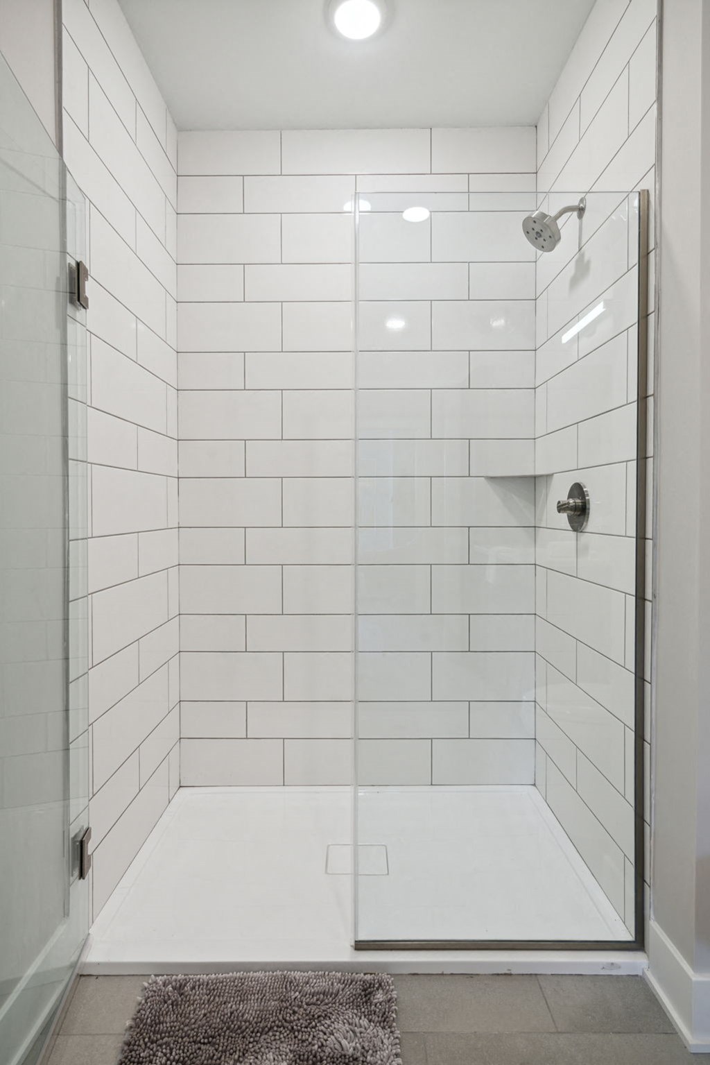 a white tiled shower in a bathroom with a glass door