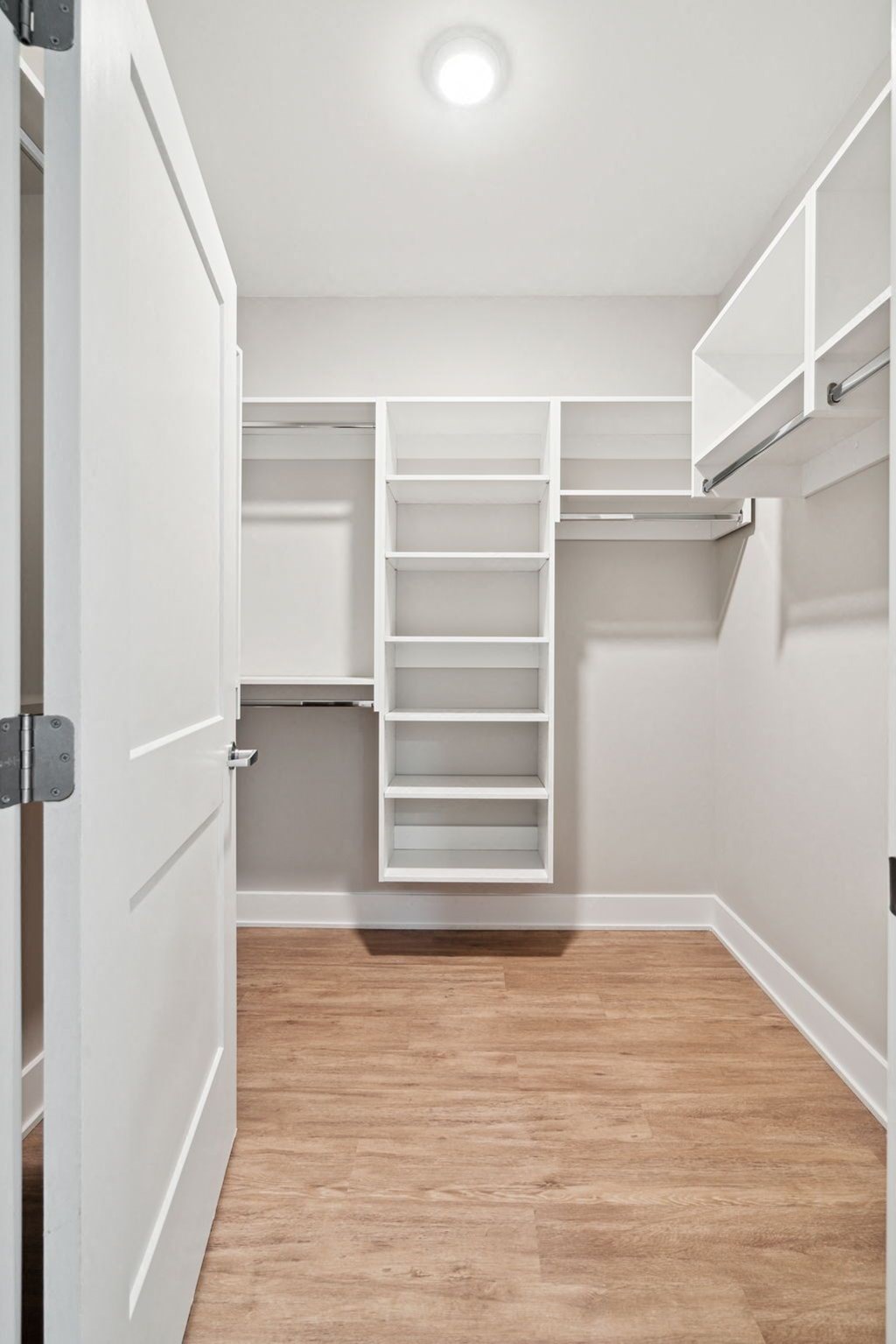 a large walk in closet with white shelves and a wood floor