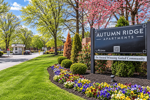 A sign for Autumn Ridge Apartments is surrounded by flowers and greenery.