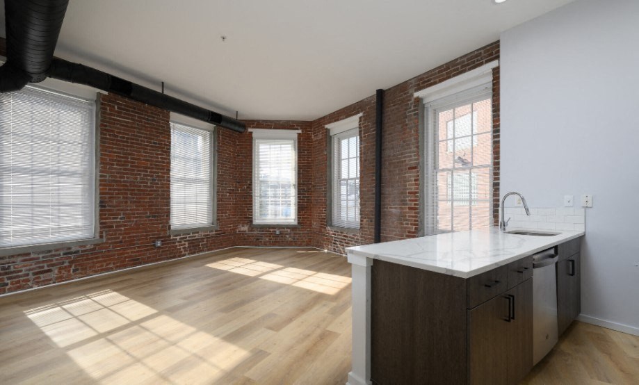 an empty living room with a large window and a kitchen