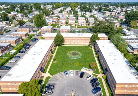 A large building complex with a green lawn in the middle and a parking lot in front.