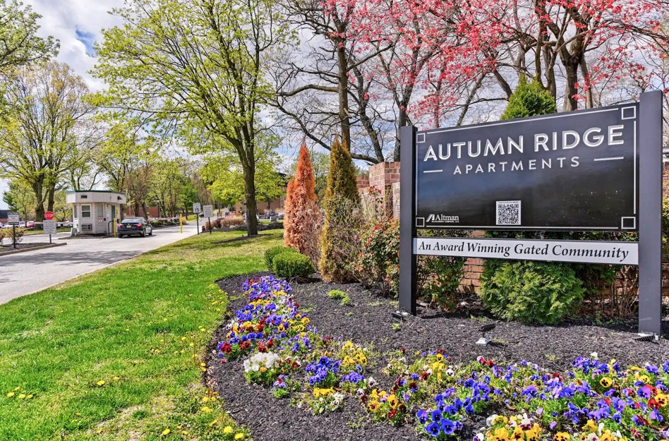A sign for Autumn Ridge Apartments is displayed in front of a flower bed.