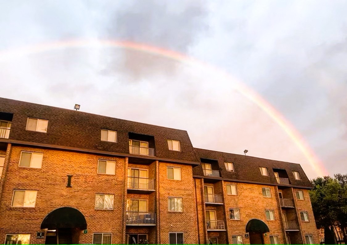 A rainbow appears over a multi-story brick building.