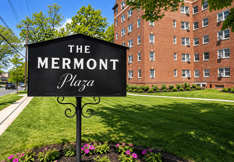 A black sign with white lettering that says "The Mermont Plaza" stands in front of a brick building.