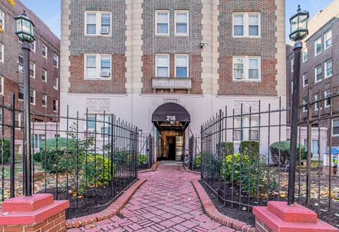 A brick pathway leads to a black iron gate entrance.