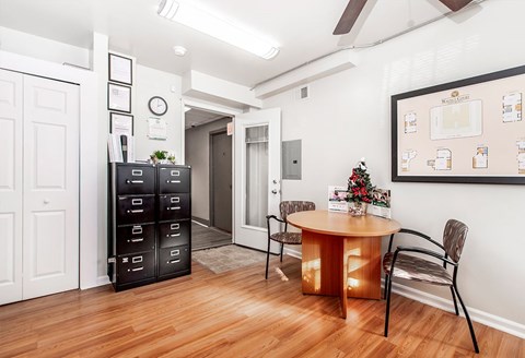 A room with a round table and chairs, a cabinet, and a wall with a clock and pictures.