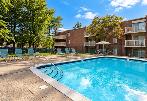 A swimming pool surrounded by chairs and trees in front of apartment buildings.