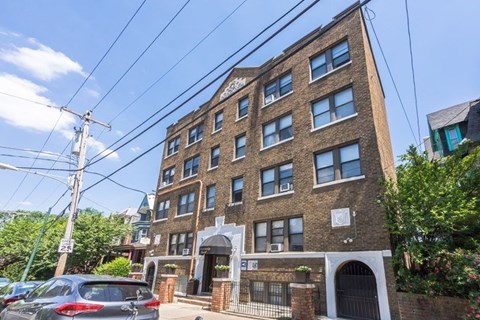 A brown brick building with a white arched entrance and a car parked in front.