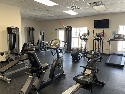 A gym with treadmills, elliptical machines, and a television.