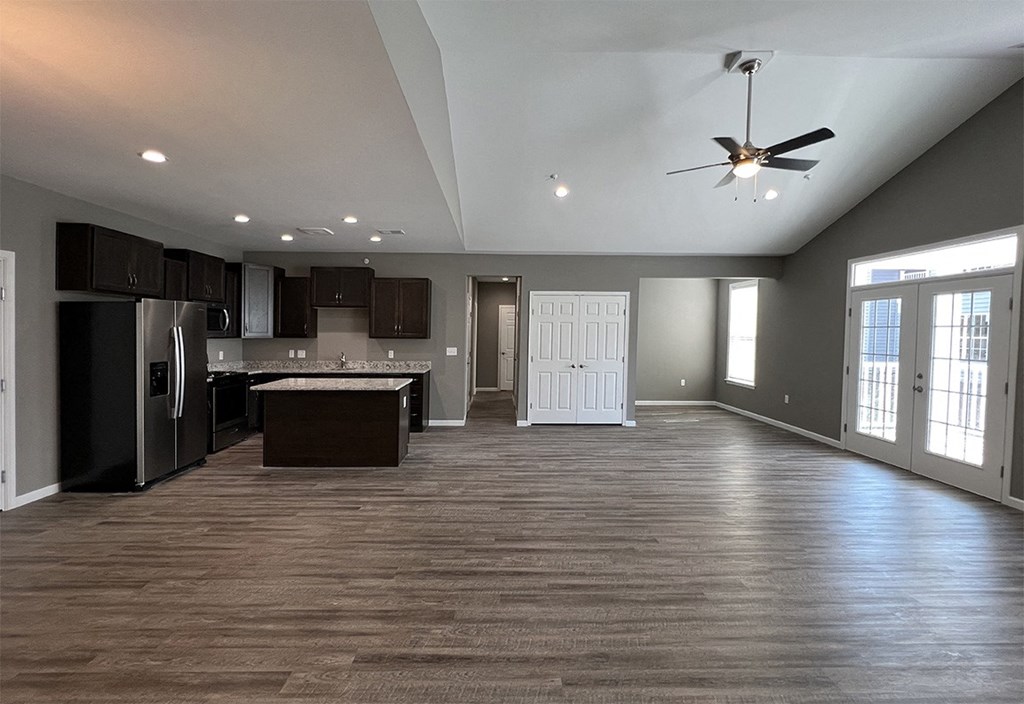 an empty living room with a kitchen and a ceiling fan