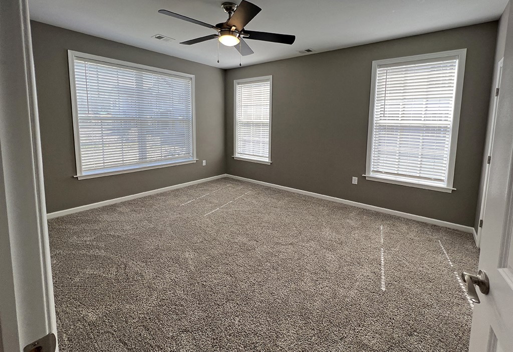 an empty room with a ceiling fan and two windows