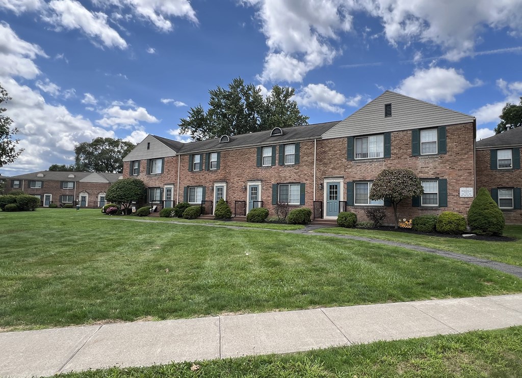 a large brick apartment building with a lawn and a sidewalk